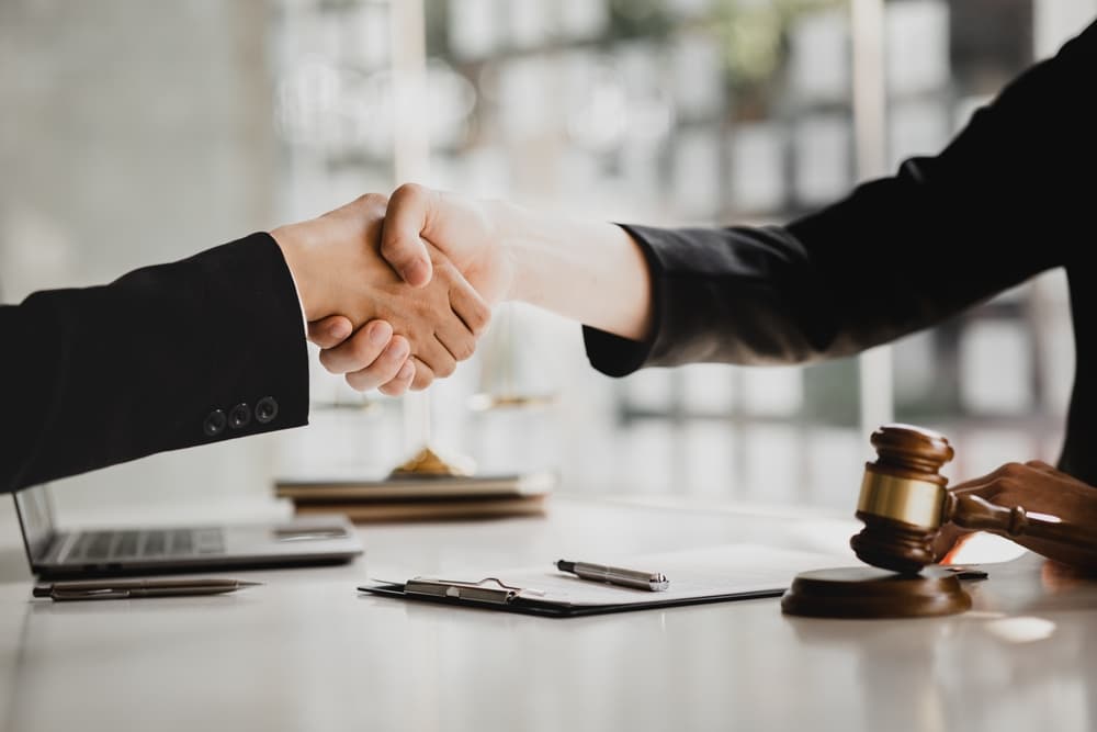A close-up of a professional handshake over a desk, with a legal gavel and documents, representing an agreement or retention of an Accident Injury Claim Lawyer.