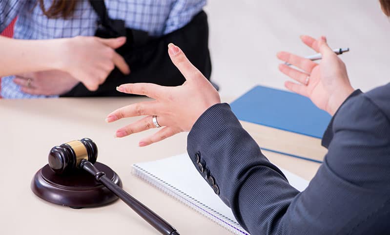 An attorney in a suit gestures while consulting with an injured client wearing an arm sling at a desk with a wooden gavel, illustrating a meeting with a Personal Injury Case Lawyer.