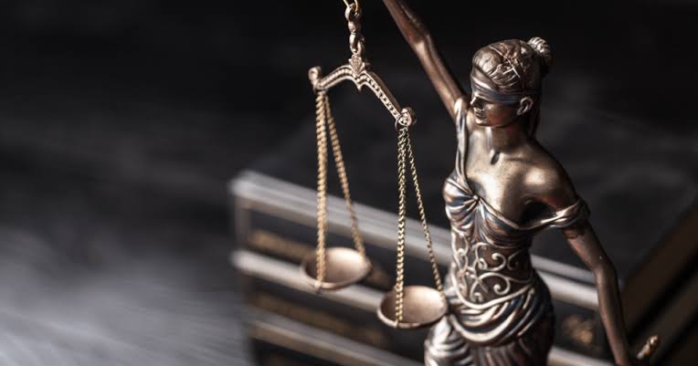 A bronze statue of Lady Justice holding the scales of justice in front of stacked legal books, representing the ethical standards upheld by a Personal Injury Attorney Firm.